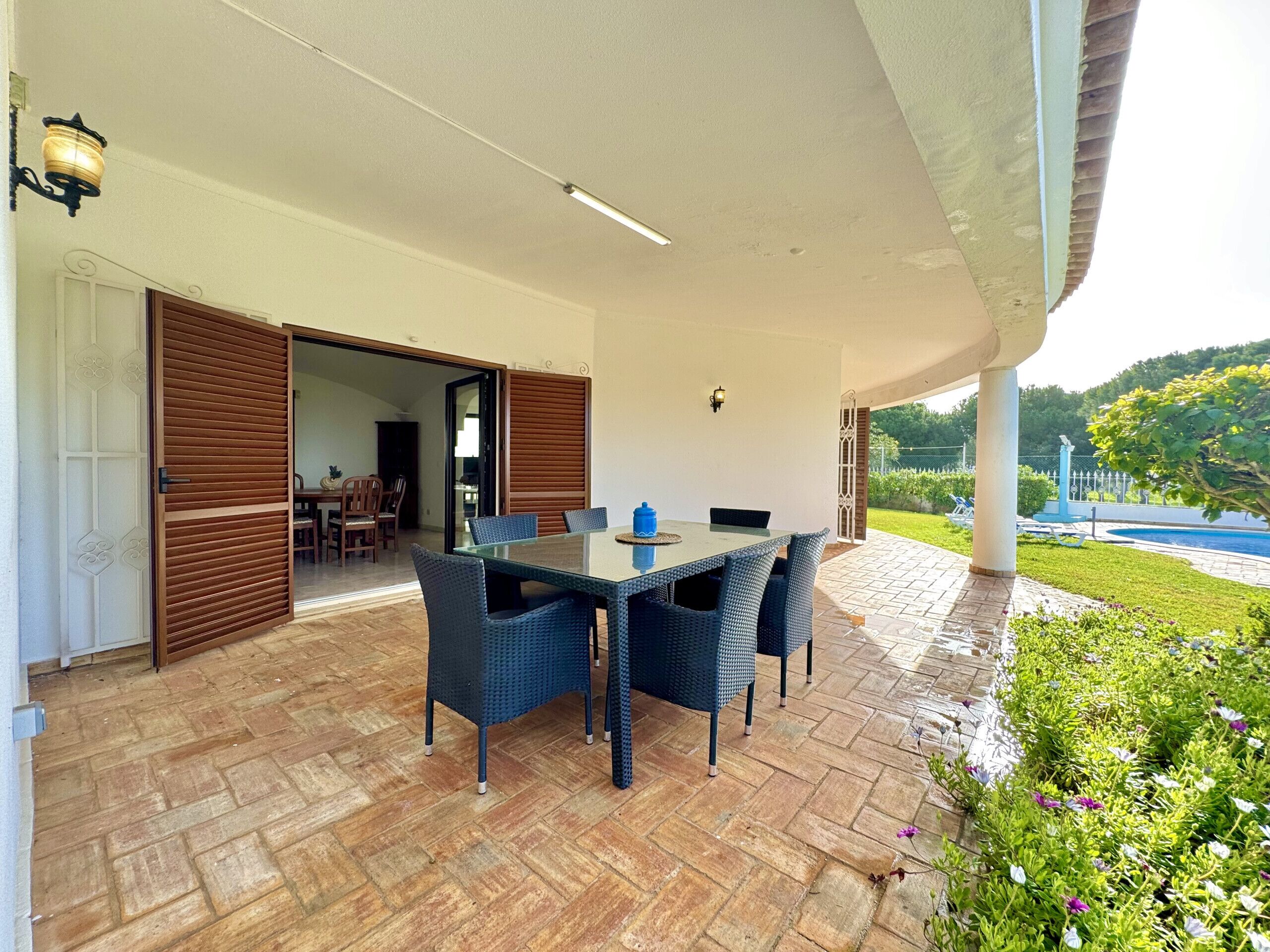 Un patio exterior con mesa y sillas, una puerta de madera y vistas a una piscina y follaje.