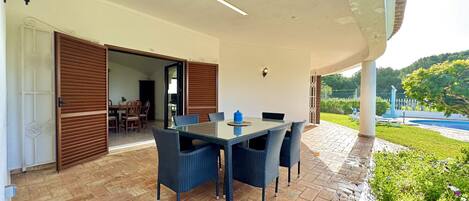 Un patio exterior con mesa y sillas, una puerta de madera y vistas a una piscina y follaje.