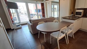 Eine kompakte Küche mit Essbereich, einer Couch und einem Fenster mit Vorhängen.