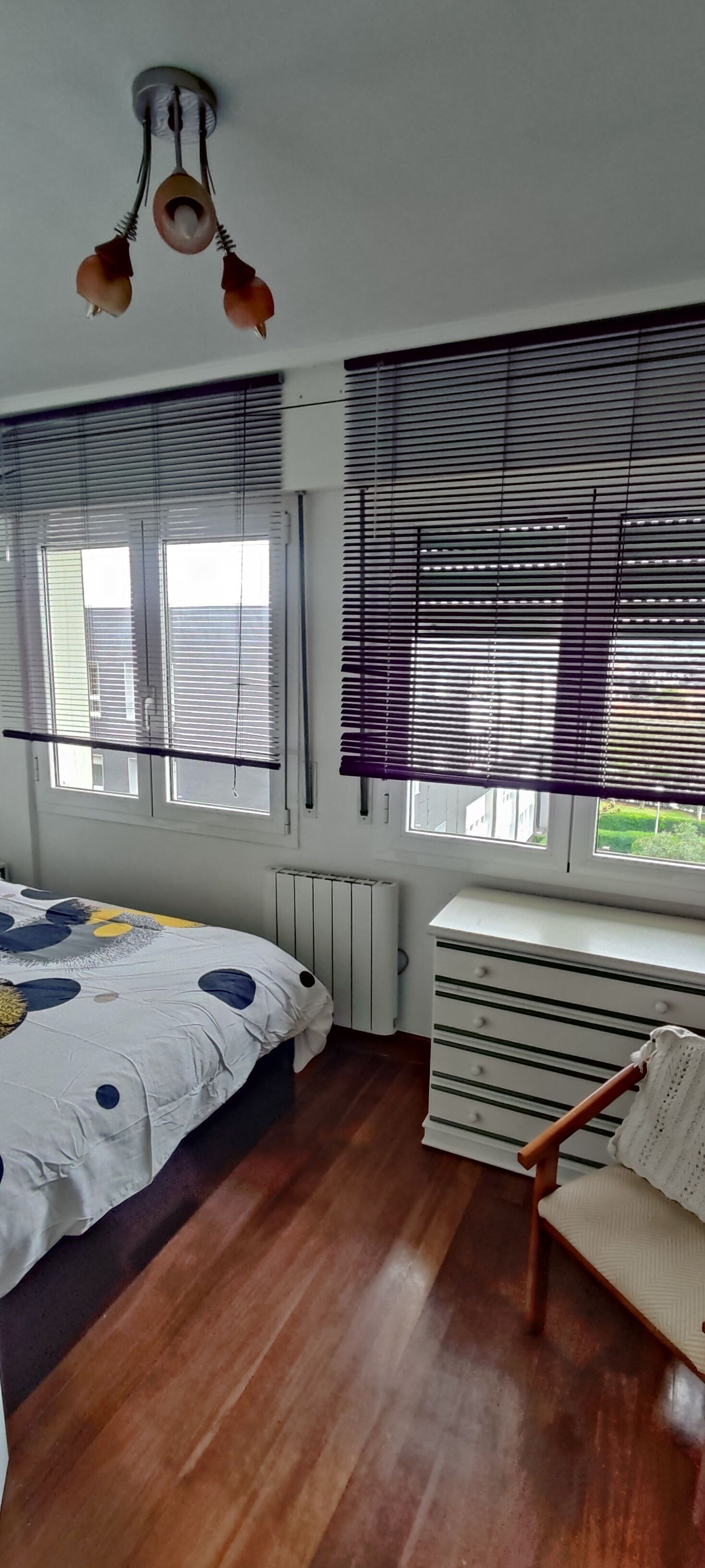 Een slaapkamer met een bed, een dressoir, een stoel en een plafondventilator.