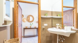 Ein Badezimmer mit Holztür, Spiegel, Waschbecken mit goldfarbenem Wasserhahn und Handtuchhalter.