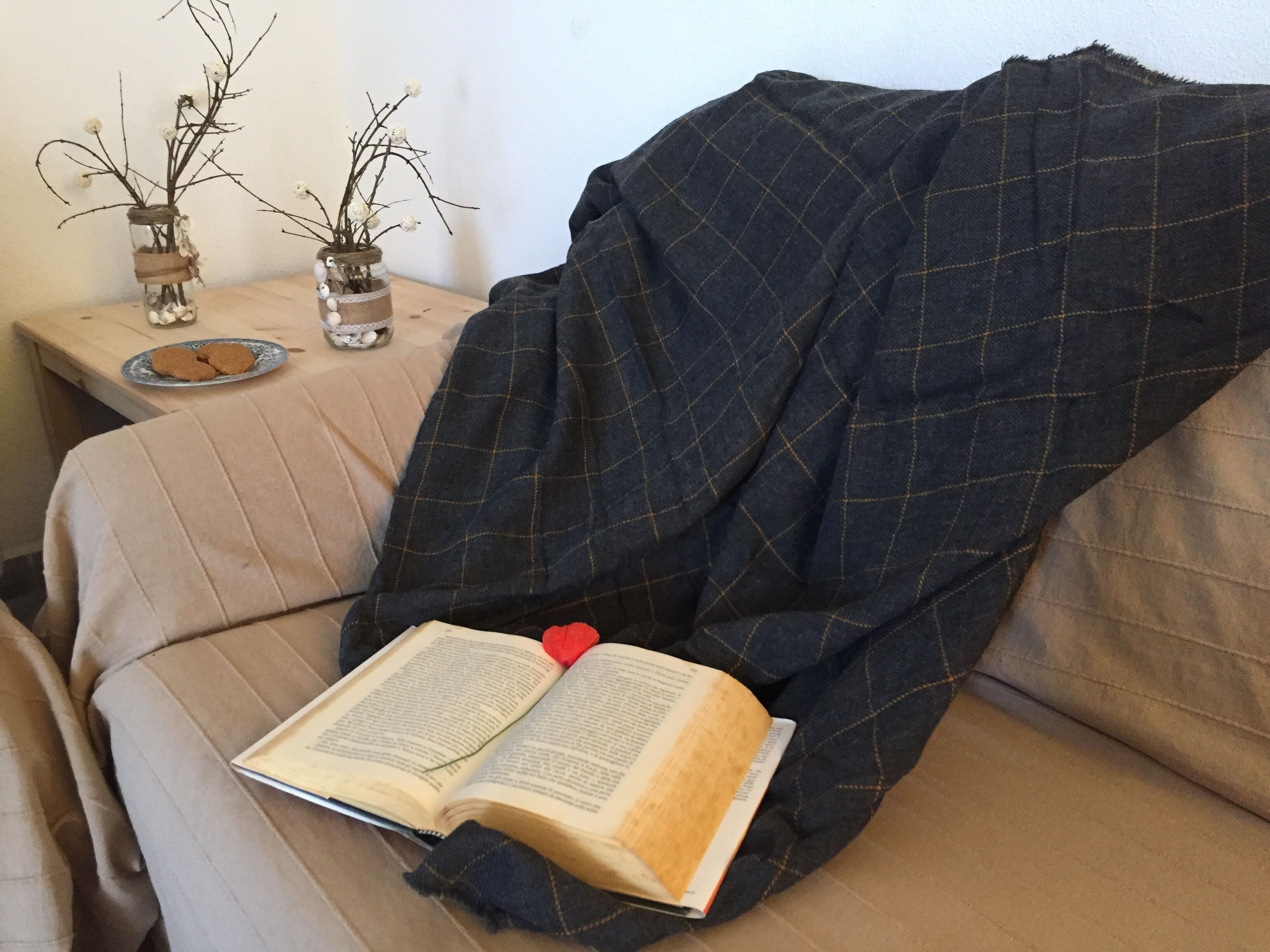A cozy reading nook with a book, a blanket, and decorative jars on a side table.