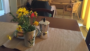 A living room with a coffee table, a vase with yellow flowers, a metal pot, and a sofa. - Sa Domo de Mannoi, home just minutes from Sardinia's most beautiful beaches (Orosei)