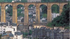 Un puerto deportivo con numerosas embarcaciones amarradas, un puente al fondo y edificios a lo largo de la costa.