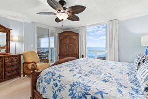 A bedroom with a large bed, a wooden dresser, a chair, a ceiling fan, and a view of the ocean. - Charming Beachfront 1065 w/Beach Service (Destin)