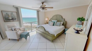 A bedroom with a bed, a chair, a nightstand, a lamp, a ceiling fan, a view of the beach, and a painting on the wall. - Beachfront Balcony Shoreline Towers 2063 (Destin)