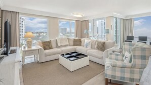 Ett modernt hotellrum med en sektionssoffa, en platt-TV, ett soffbord och stora fönster med utsikt över staden.