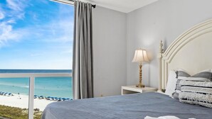 A hotel room with a bed, a nightstand with a lamp, and a view of the beach and ocean. - Gorgeous ST 2073 w/Beach Service (Destin)