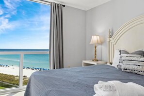 A hotel room with a bed, a nightstand with a lamp, and a view of the beach and ocean. - Gorgeous ST 2073 w/Beach Service (Destin)