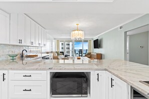 A modern kitchen with white cabinetry, a central island, and a built-in microwave. - Gorgeous ST 2073 w/Beach Service (Destin)