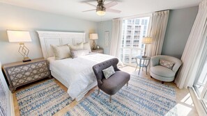 A hotel room with a large bed, two nightstands, a chair, a small table, and a view of the city. - Stunning Shoreline Towers 2094 (Destin)