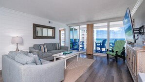 Een woonkamer met een bank, salontafel en uitzicht op de oceaan door grote glazen schuifdeuren.