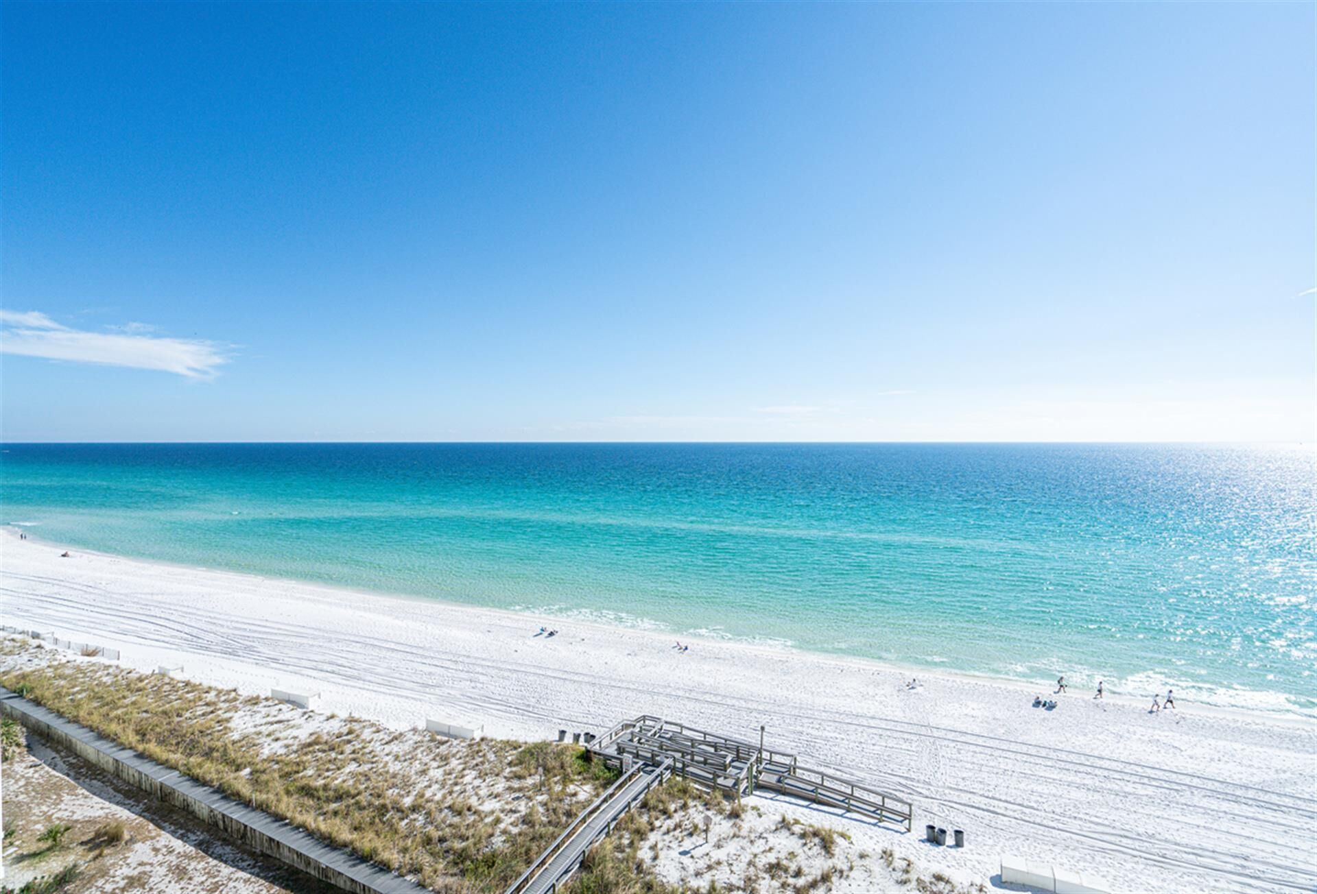 A beach with a clear sky, sandy shore, and a wooden walkway leading to the water.