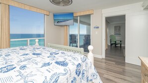 Een slaapkamer met een bed, een plafondventilator, een televisie en uitzicht op de oceaan.