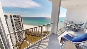 A balcony with a view of the beach and ocean, a table with chairs, and a wicker chair with a cushion. - 2122 is a Gulf Front 3 bedroom w/Beach Service. (Destin)