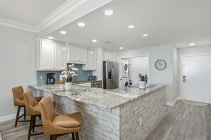A modern kitchen with white cabinets, a marble island, and a built-in oven. - Penthouse 2123 w/Beach Service (Destin)