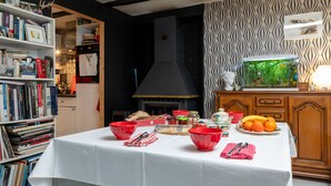 Un comedor con una mesa dispuesta para una comida, rodeado de estanterías y una zona de cocina con chimenea.