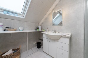 A small, modern bathroom with a skylight, white tiles, a sink, and a mirror.
