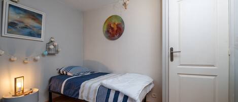 A bedroom with a bed, a nightstand, a wall-mounted picture, a door, and a ceiling light fixture.