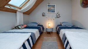 Un dormitorio con dos camas, un tragaluz, una mesita de noche con lámpara y un cuadro colgado en la pared.