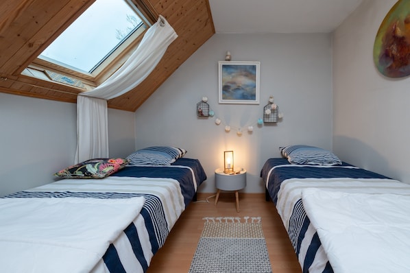 A bedroom with two beds, a skylight, a nightstand with a lamp, and a wall-mounted picture.