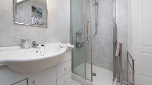 Un baño con un lavamanos blanco, cabina de ducha de vidrio y una puerta blanca.