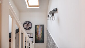 Un pasillo con tragaluz, un reloj de pared y un cuadro abstracto enmarcado.