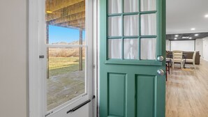Um quarto com porta verde, janela, teto de madeira e vista para uma área gramada.