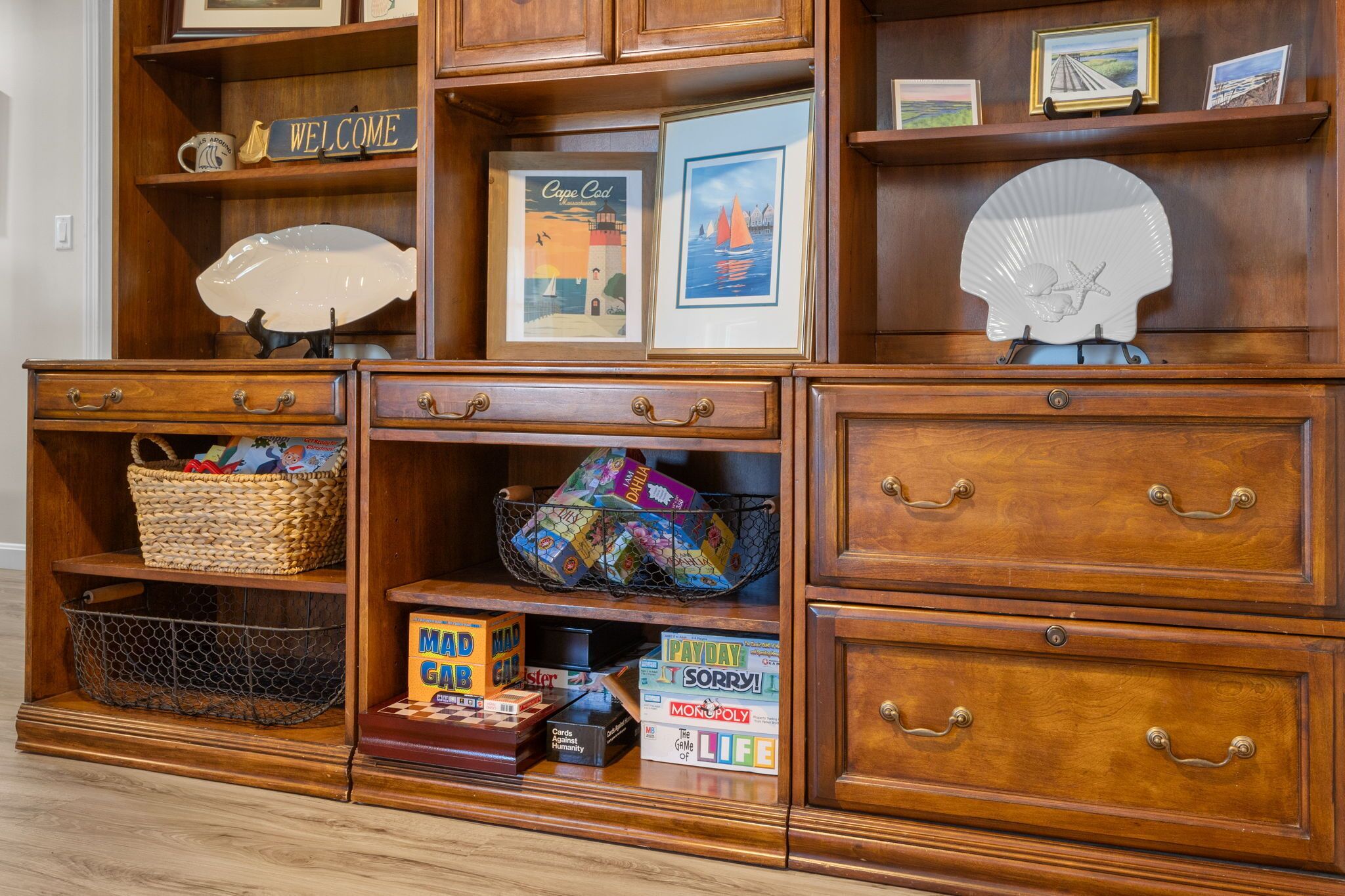 A wooden cabinet with drawers, shelves, and a basket containing board games.