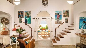 A spacious living area with a staircase leading to an outdoor terrace, decorated with various artworks and a central archway. - Seafront Casa Azul Villa - Getaway in Kalymnos (Mirties)