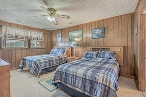 A bedroom with two beds, wooden walls, a ceiling fan, and framed artwork. - Loafers Lodge - Channel Home (North Myrtle Beach)