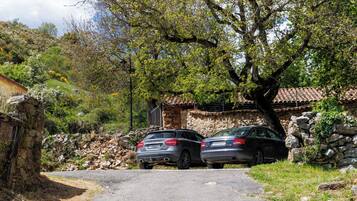 Two cars parked in front of a stone building with a tiled roof, surrounded by trees and a stone wall.