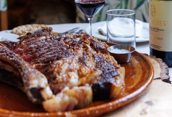 A plate of grilled steak with a side of bread, a glass of red wine, and a bottle of wine. - El Refugio II de Verdiago (Cremenes)