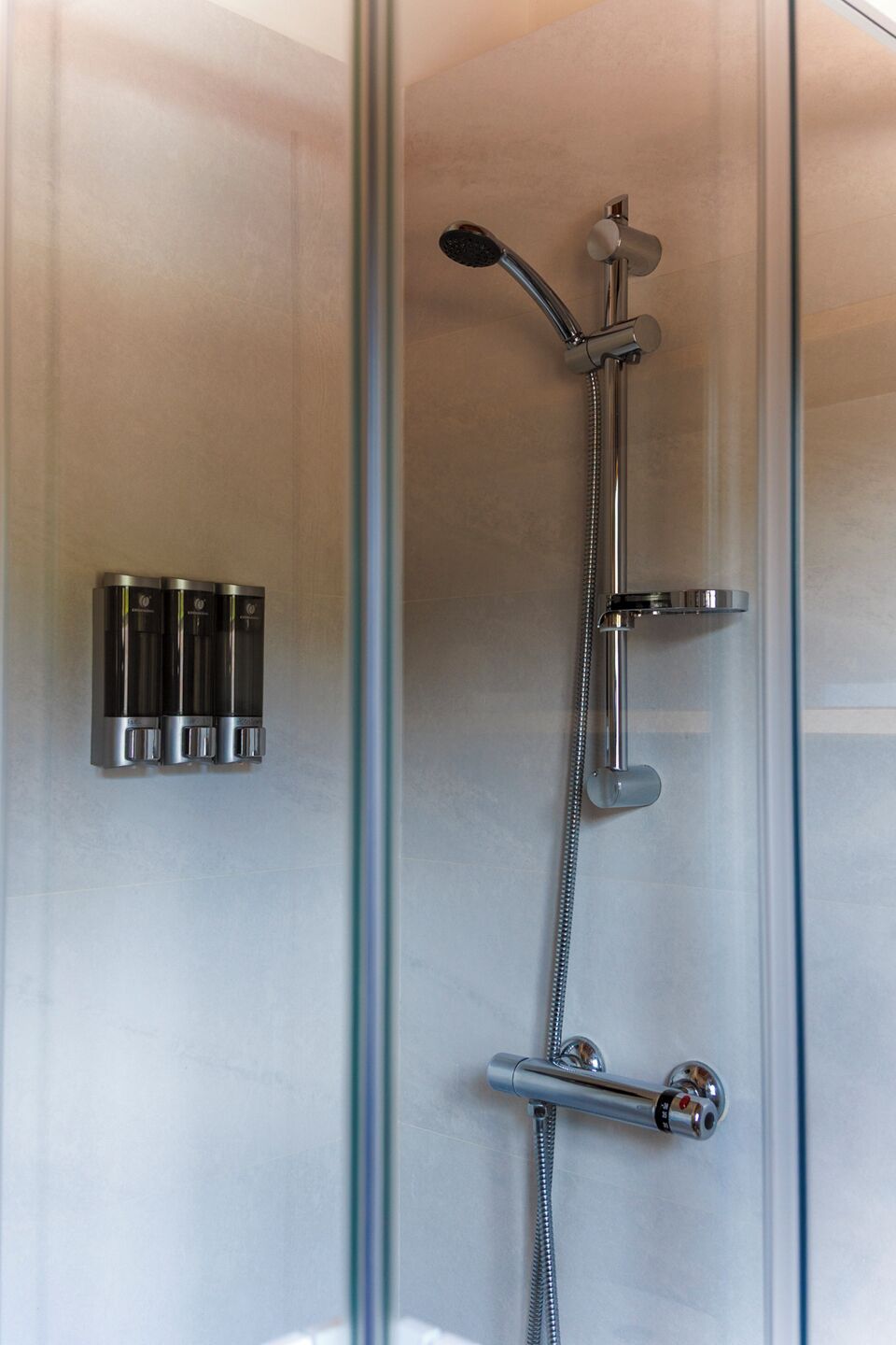 Une douche moderne dotée d’un pommeau de douche à main et d’un robinet mural.