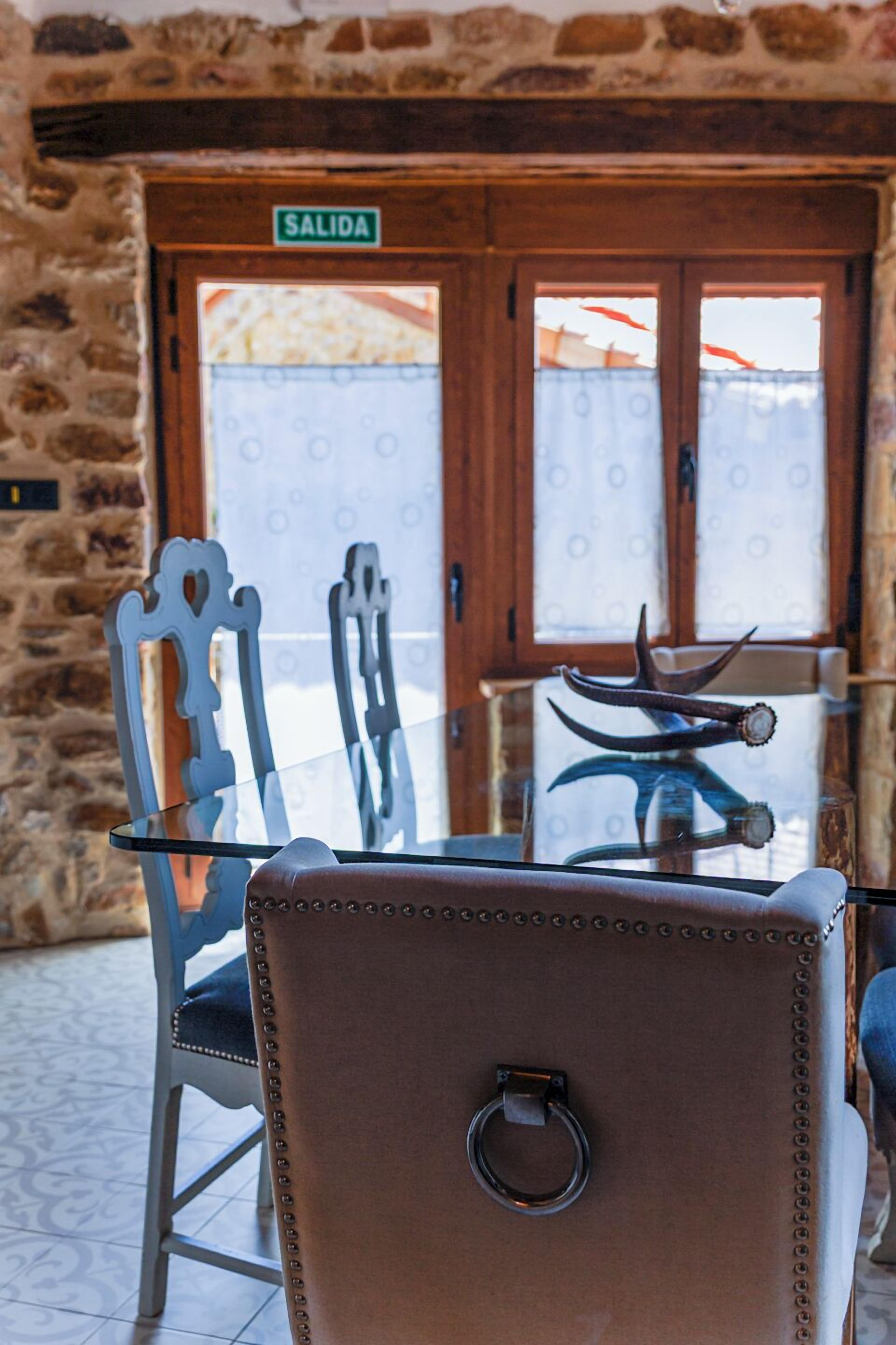 Una mesa con cubierta de vidrio y una silla con respaldo de cuero frente a una pared de piedra.
