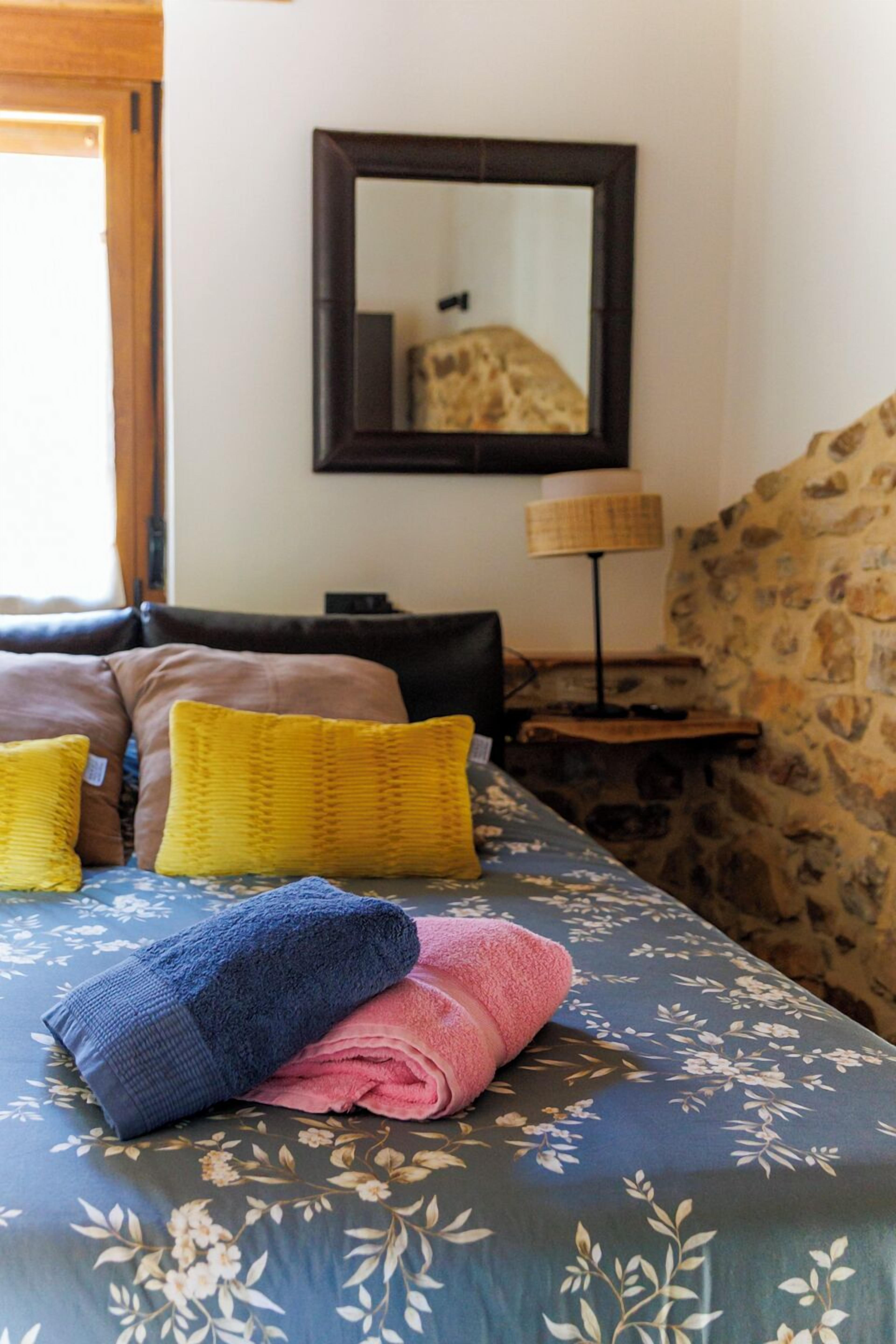 Una cama con ropa de cama floral, un espejo, una lámpara y una pared de piedra.