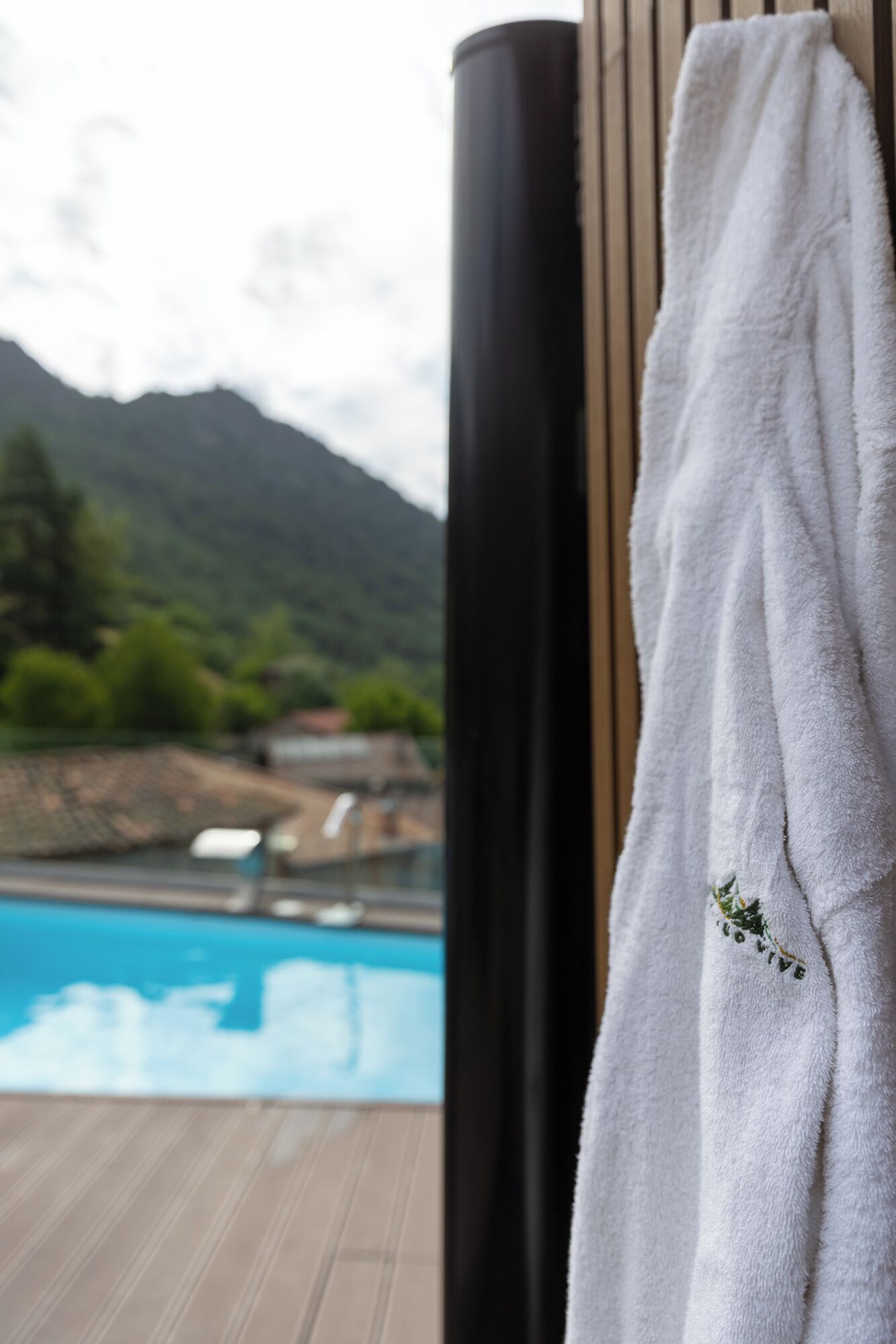 A white towel hanging on a wooden wall with a view of a swimming pool and mountains in the background.