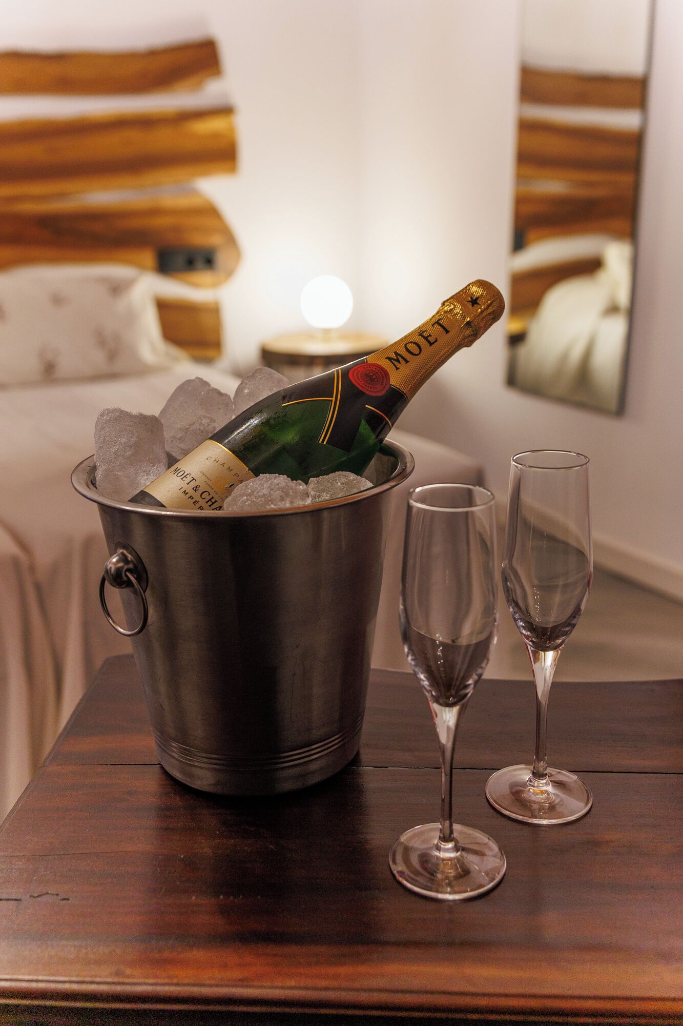 A minibar with a bottle of champagne and ice, and two empty glasses on a wooden table in a hotel room.
