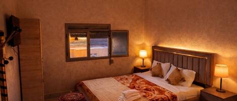 A bedroom with a large bed, bedside tables with lamps, a window, and a wardrobe.
