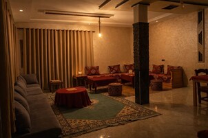 Una habitación de hotel con un sofá, dos mesas, una alfombra y un pilar grande.