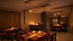 Un restaurant à la lumière tamisée, avec de nombreuses tables et chaises, des bougies sur chaque table et une atmosphère chaleureuse.
