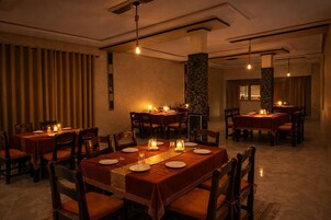 Un restaurante tenuemente iluminado con varias mesas y sillas, velas en cada mesa y un ambiente cálido.