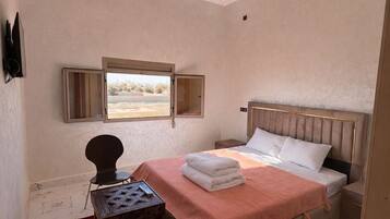 A bedroom with a bed, a small table, a chair, and a window.
