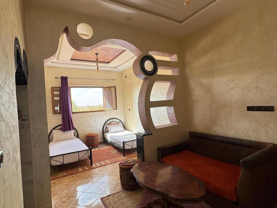 A living room with a sofa, a small table, a patterned rug, and a bed with a window view.