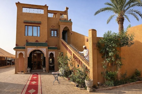 A traditional building with a staircase, a palm tree, and a red carpet leading to the entrance.