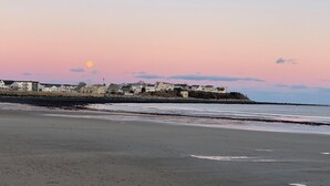 Paesaggio costiero con file di case lungo la riva, una spiaggia in primo piano e un tramonto sullo sfondo.