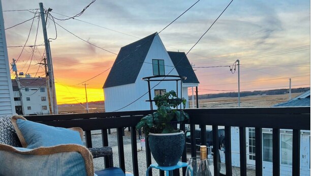 Un balcone con una sedia, un tavolo con una bottiglia di vino e una pianta in vaso.