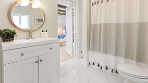 Un bagno con un mobile lavabo bianco, uno specchio rotondo illuminato, un water e una tenda da doccia con frange.