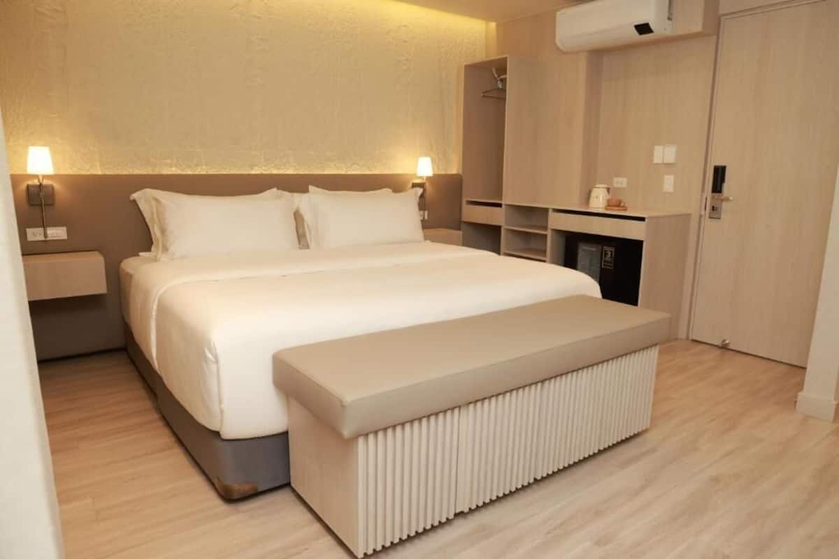 A modern hotel room with a large bed, bedside tables, a built-in bench, and a wardrobe.