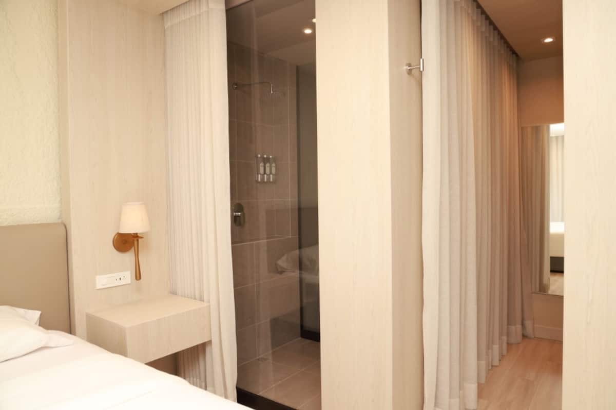 A modern hotel room with a shower area, a bedside table with a lamp, and a bed.